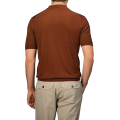 A man wearing a Brick Red Knitted Silk Polo Shirt by Gran Sasso and beige pants stands with his back to the camera, showcasing the essence of a refined summer wardrobe.