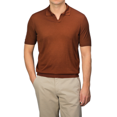 A person wearing a Brick Red Knitted Silk Polo Shirt by Gran Sasso and beige pants stands with one hand in their pocket against a neutral background, showcasing a refined summer wardrobe.