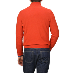 Back view of a person wearing the Gran Sasso Bright Orange Cashmere 1/4 Zip Sweater and dark blue jeans, standing against a plain background, showcasing the elegance of premium knitwear.