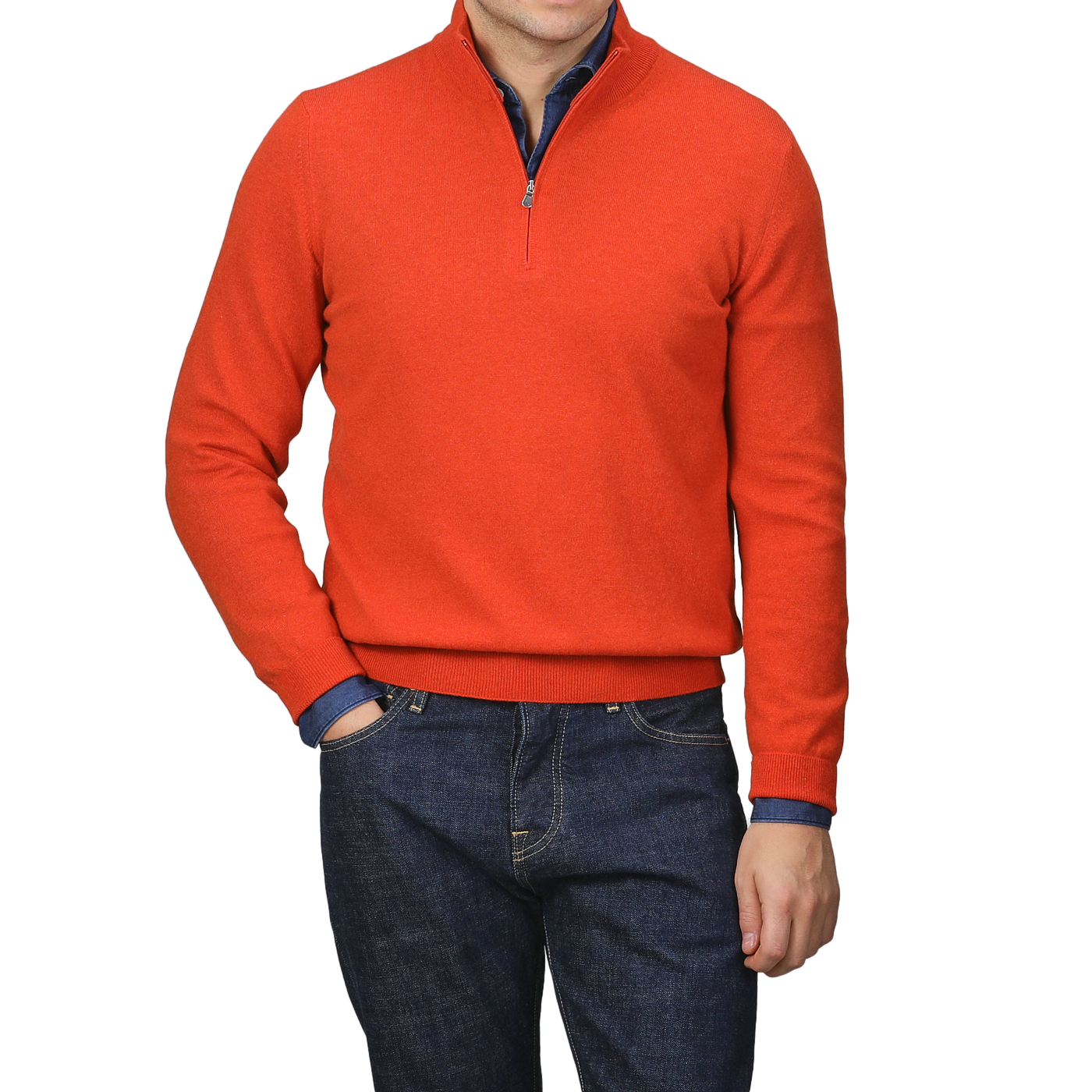 A person wearing a bright orange cashmere 1/4 zip sweater from Gran Sasso and dark blue jeans stands with one hand in a pocket, exuding the elegance of premium knitwear.