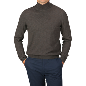 Person wearing a Brown Melange Merino Wool Roll Neck by Gran Sasso and blue pants, posing with hands in pockets against a plain background.