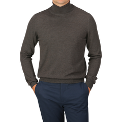 Person wearing a Brown Melange Merino Wool Roll Neck by Gran Sasso and blue pants, posing with hands in pockets against a plain background.