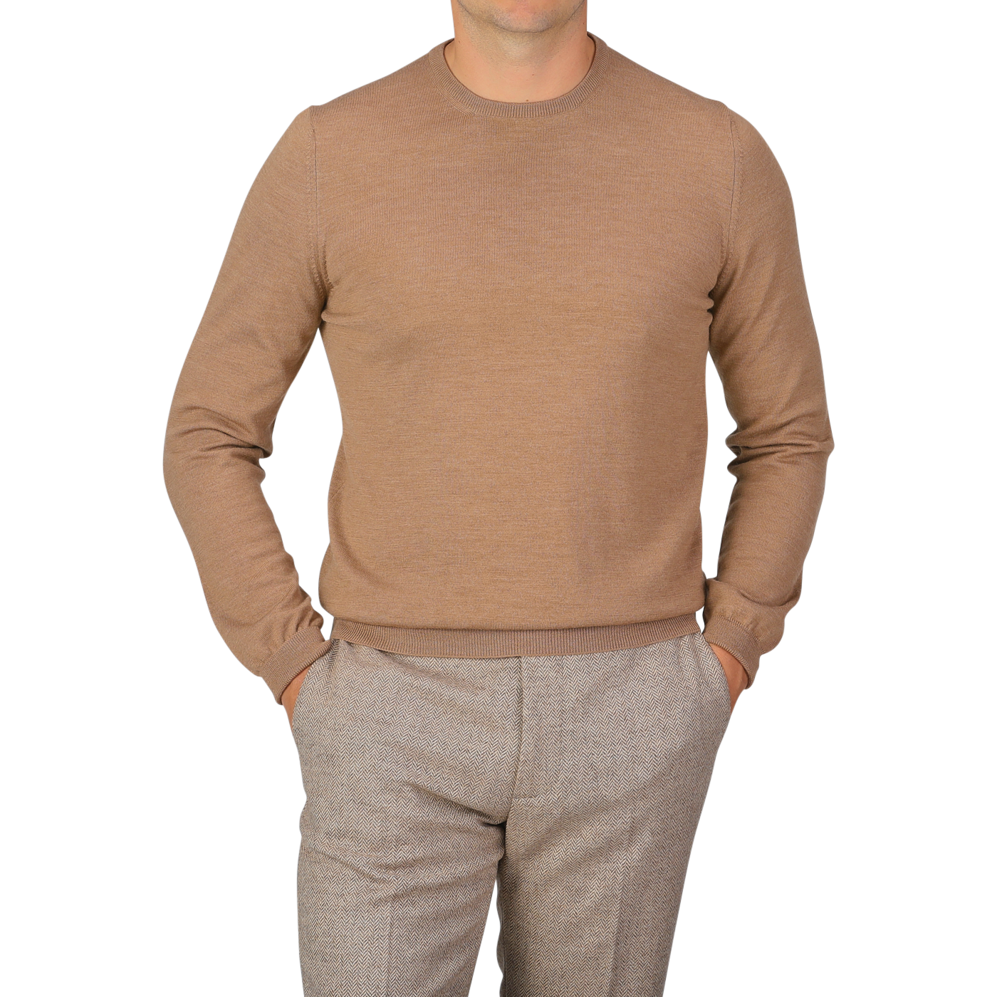 A person wearing a Camel Beige Extra Fine Merino Crew Neck by Gran Sasso and gray pants, with hands in pockets, standing against a plain backdrop.