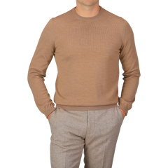 A person wearing a Camel Beige Extra Fine Merino Crew Neck by Gran Sasso and gray pants, with hands in pockets, standing against a plain backdrop.