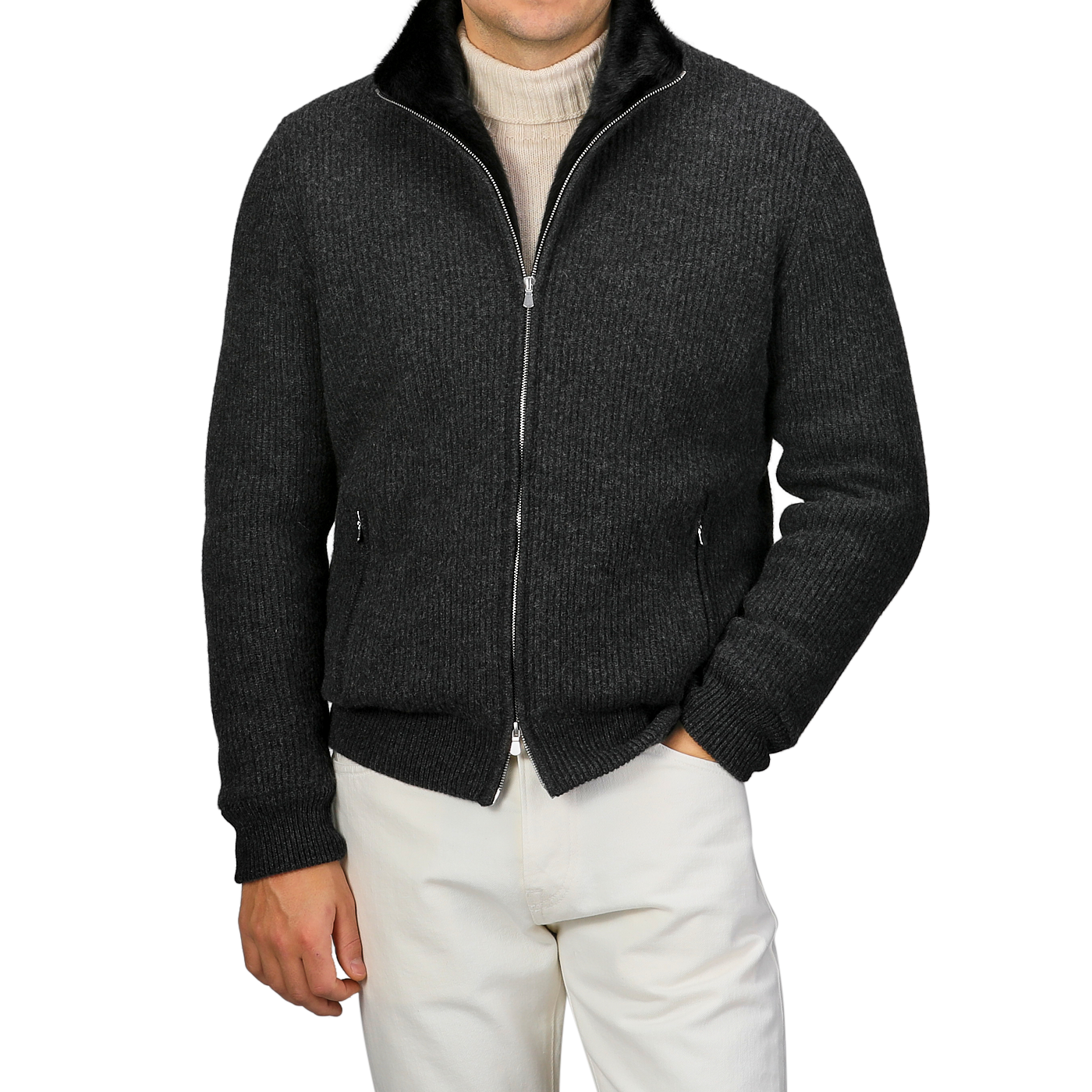 A person wearing a Charcoal Faux Fur Lined Cashmere Blouson by Gran Sasso over a light turtleneck sweater and white pants stands with hands in the jacket pockets against a plain background.