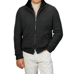 A person wearing a Charcoal Faux Fur Lined Cashmere Blouson by Gran Sasso over a light turtleneck sweater and white pants stands with hands in the jacket pockets against a plain background.