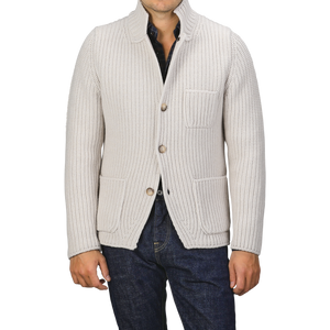 A man is wearing a Cream Beige Chunky Knitted Wool Cardigan by Gran Sasso, featuring a shawl collar and large front pockets, over a dark shirt and blue jeans. His face is not shown.