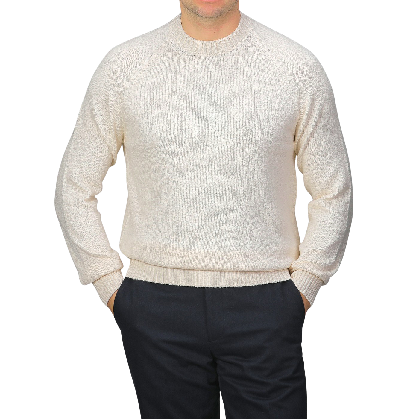 Dressed in Gran Sasso's Cream Cotton Boucle Crewneck Sweater and dark pants, a person with hands in pockets stands against a plain grey background. The pure cotton boucle fabric of the sweater adds texture to the simple outfit.