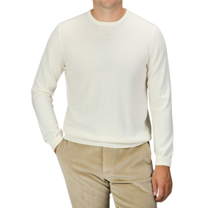 A person wearing the Cream Extra Fine Merino Crew Neck and beige corduroy pants from Gran Sasso, with their hand in their pocket, against a black background.