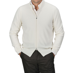 A person in a Gran Sasso Cream Felted Cashmere Zip Cardigan with hands in pockets, wearing brown pants against a grey background. The contemporary fit sweater showcases an effortlessly stylish look, though the person's head is not visible.