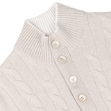 Close-up of a cream pure cashmere quarter button sweater featuring a cable-knit design, high ribbed collar, and three vertically aligned beige buttons in the front. Crafted with impeccable care, this Gran Sasso creation exudes timeless elegance.