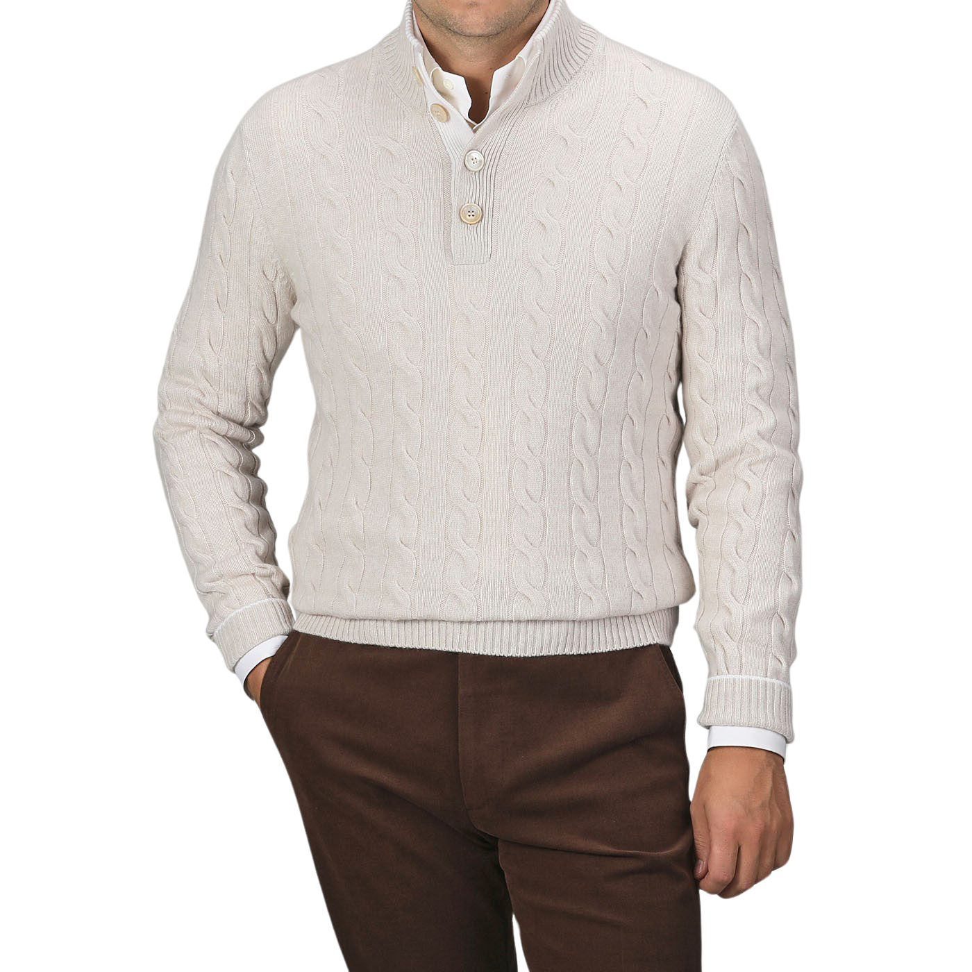 A man is wearing a cream Pure Cashmere Quarter Button Sweater by Gran Sasso over a white button-up shirt, paired with brown trousers. The top button of the cable-knitted sweater is undone. The background is plain gray.