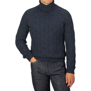 A person is wearing a dark blue Gran Sasso Wool Cable Knit Rollneck sweater, made from pure virgin wool, and dark jeans, posing with one hand in their pocket.