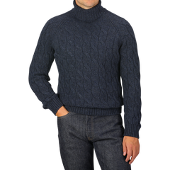 A person is wearing a dark blue Gran Sasso Wool Cable Knit Rollneck sweater, made from pure virgin wool, and dark jeans, posing with one hand in their pocket.