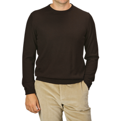 A person is wearing the Gran Sasso Dark Brown Extra Fine Merino Crew Neck long-sleeve sweater and beige pants with their right hand in their pocket, showcasing a versatile wardrobe. The person's head is not visible.