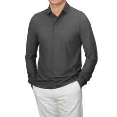 Wearing a Gran Sasso Dark Grey Washed Cotton Popover Shirt with white pants, an individual stands against a neutral background. The slim fit of the pure cotton jersey accentuates their silhouette as they casually rest their hands in their pockets.