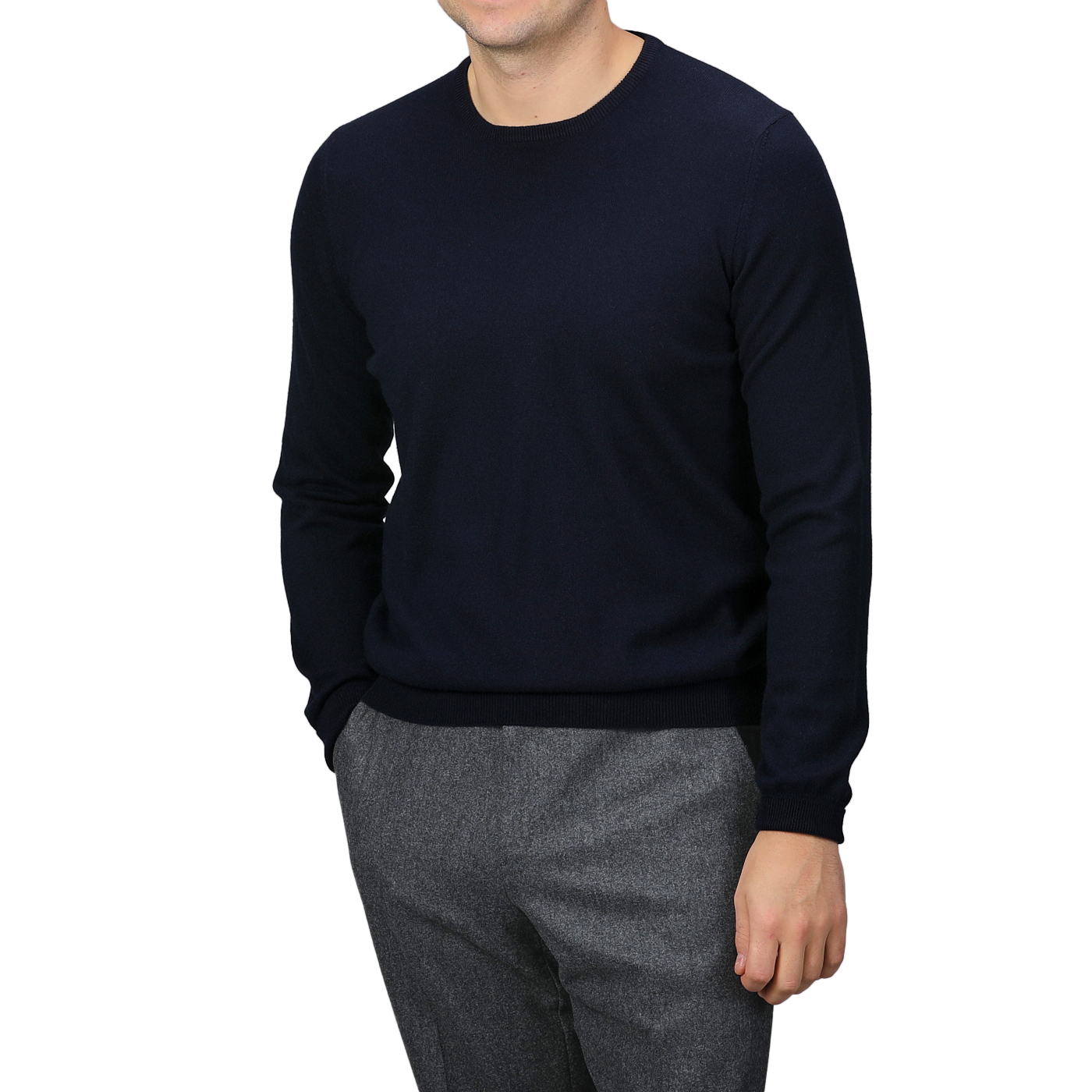 A person wearing a Dark Navy Cashmere Crewneck Sweater by Gran Sasso, along with gray trousers, stands against a plain background with hands in pockets.