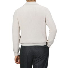 A person facing away, wearing a Gran Sasso Ecru Beige Chunky Knit Wool Polo Shirt made of super Geelong wool and dark trousers. The background is plain and neutral.