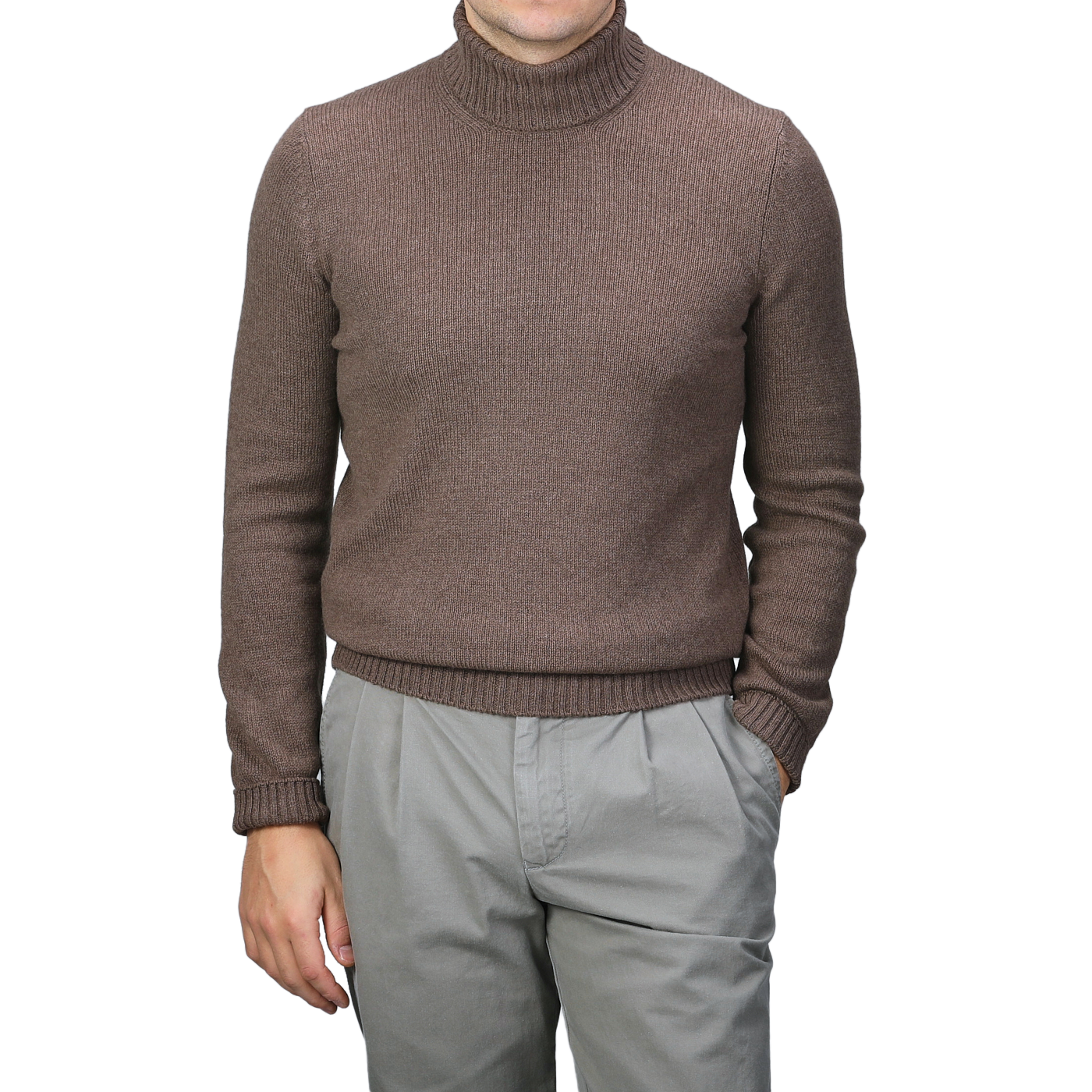 A person dressed in a Gran Sasso Fawn Brown Air Wool Rollneck and gray pants stands with one hand in a pocket against a plain backdrop.