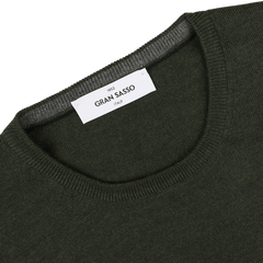 A close-up of the Green Melange Extra Fine Merino Crew Neck sweater highlights its "Gran Sasso" label on the collar, underscoring its premium merino quality.