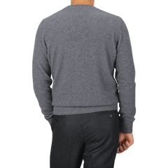 A person is shown from the back wearing a Grey Felted Cashmere Crewneck Sweater from Gran Sasso and dark grey pants, with their right hand resting on their side.