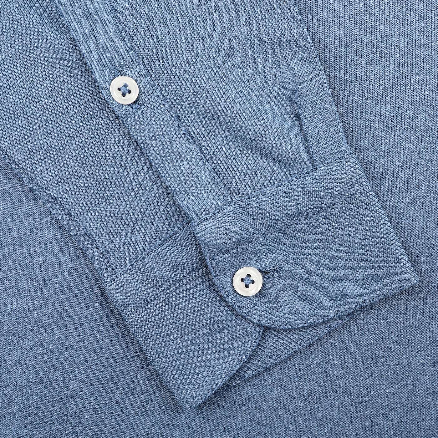 Close-up of a cuff on Gran Sasso's Indigo Blue Washed Cotton Popover Shirt, made of pure jersey with two white buttons, laid flat on matching blue fabric.