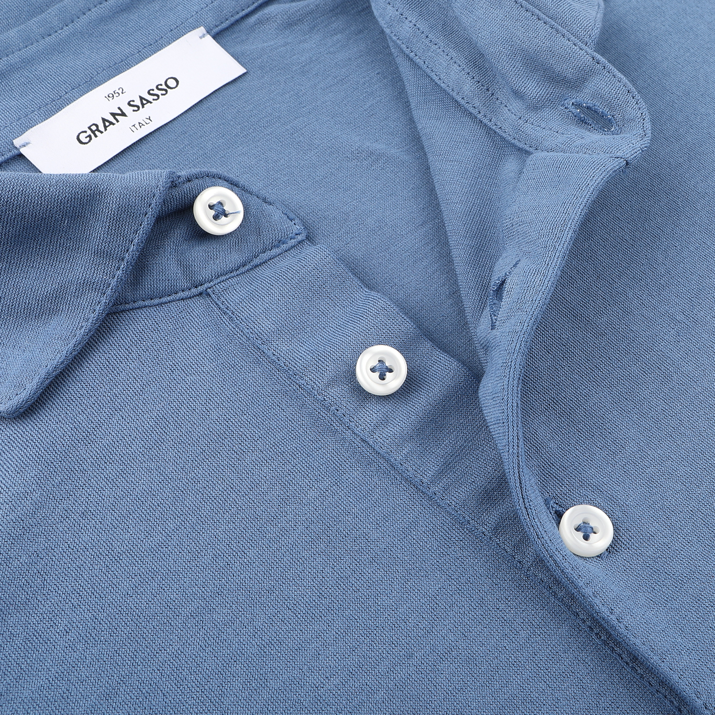 Close-up of an Indigo Blue Washed Cotton Popover Shirt by Gran Sasso, featuring white buttons and a collar. A label with "Gran Sasso" is visible, showcasing its pure cotton jersey craftsmanship.