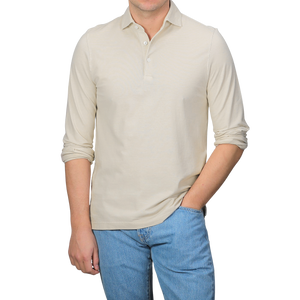 A man in a Gran Sasso Light Beige Washed Cotton Popover Shirt and blue jeans stands with his right hand in his pocket against a plain background.