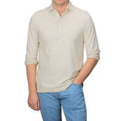 A man in a Gran Sasso Light Beige Washed Cotton Popover Shirt and blue jeans stands with his right hand in his pocket against a plain background.