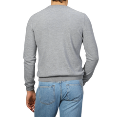 A person in a Light Grey Extra Fine Merino Crew Neck by Gran Sasso and blue jeans stands facing away, highlighting a casual yet polished look.