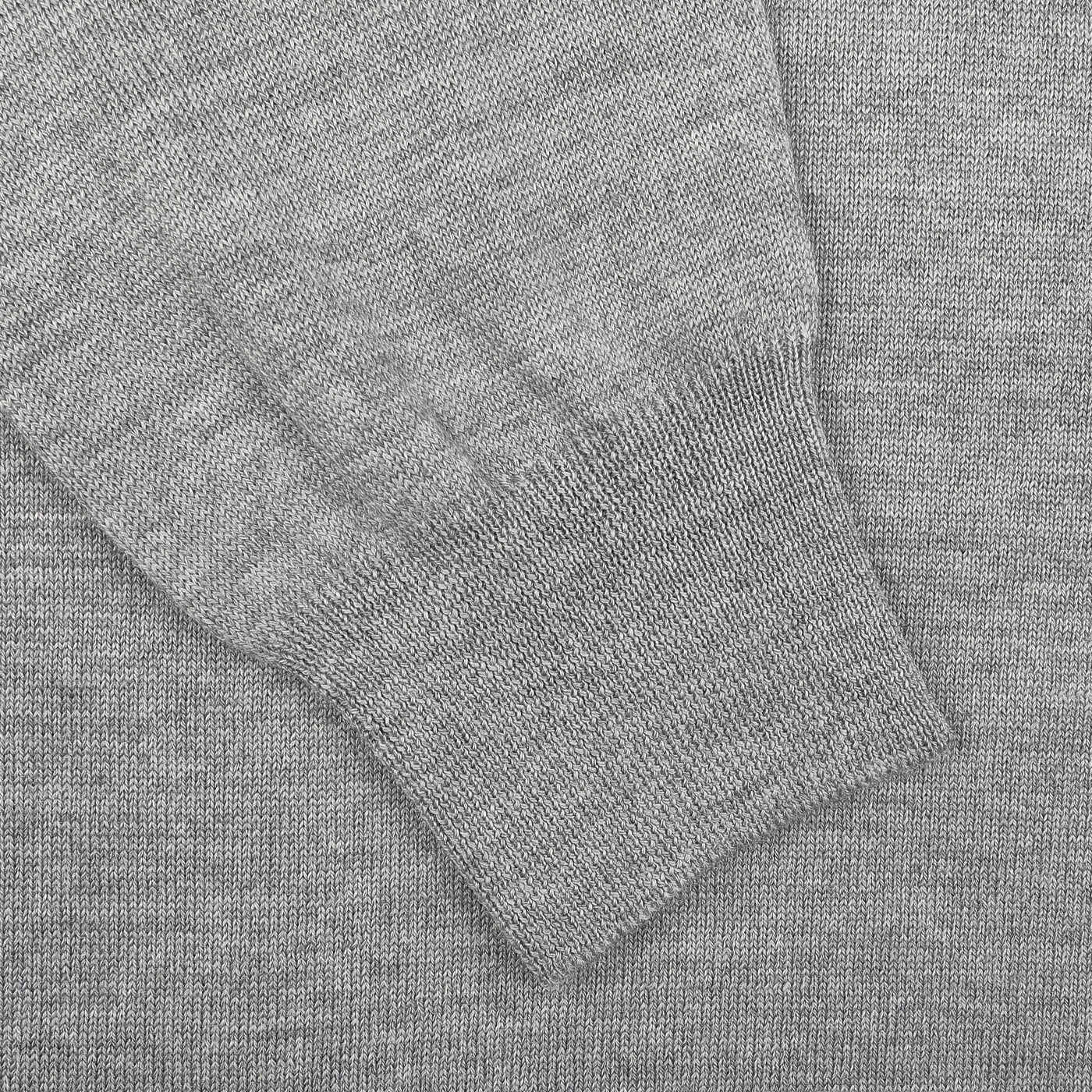 A close-up shows the elegance of a Light Grey Extra Fine Merino Crew Neck by Gran Sasso, with its ribbed sleeve on a matching knit sweater fabric background, perfect for modern business attire.