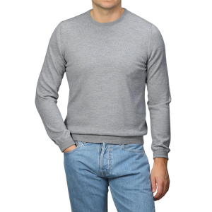 A person wearing a Gran Sasso Light Grey Extra Fine Merino Crew Neck and blue jeans stands against a gray background.