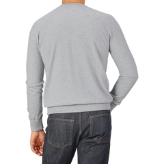 A person wearing a Gran Sasso Light Grey Wool Cashmere College Sweater and dark jeans is shown from the back, with their left hand in their pocket.