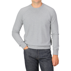 A person wearing a Light Grey Wool Cashmere College Sweater by Gran Sasso and dark jeans, standing with one hand in their pocket against a plain background.