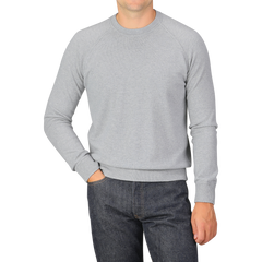 A person wearing a Light Grey Wool Cashmere College Sweater by Gran Sasso and dark jeans, standing with one hand in their pocket against a plain background.