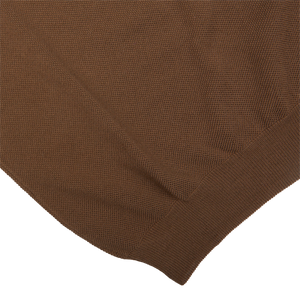 Close-up of a textured Mid-Brown Fresh Cotton Mesh Polo Shirt fabric by Gran Sasso with folded edge on a white background, highlighting its breathability.
