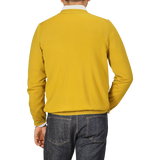 A person wearing a Mustard Yellow Extra Fine Merino Cardigan by Gran Sasso and dark jeans is photographed from behind.