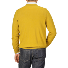 A person wearing a Mustard Yellow Extra Fine Merino Cardigan by Gran Sasso and dark jeans is photographed from behind.