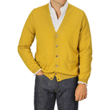 A person wearing a Gran Sasso Mustard Yellow Extra Fine Merino Cardigan, paired with a white shirt and dark jeans. The cardigan features buttons and two front pockets.