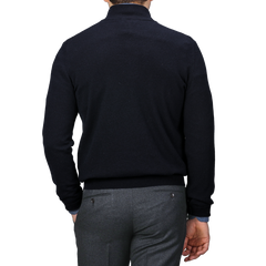 A person is shown from the back, wearing a luxurious Gran Sasso navy blue cashmere 1/4 zip sweater paired with gray pants against a monochromatic gray background.