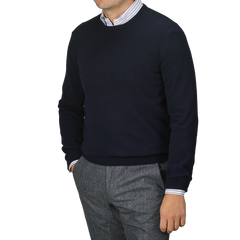 A person wearing a Gran Sasso Navy Blue Cashmere Crewneck Sweater over a striped shirt and gray trousers, standing with one hand in the pocket.