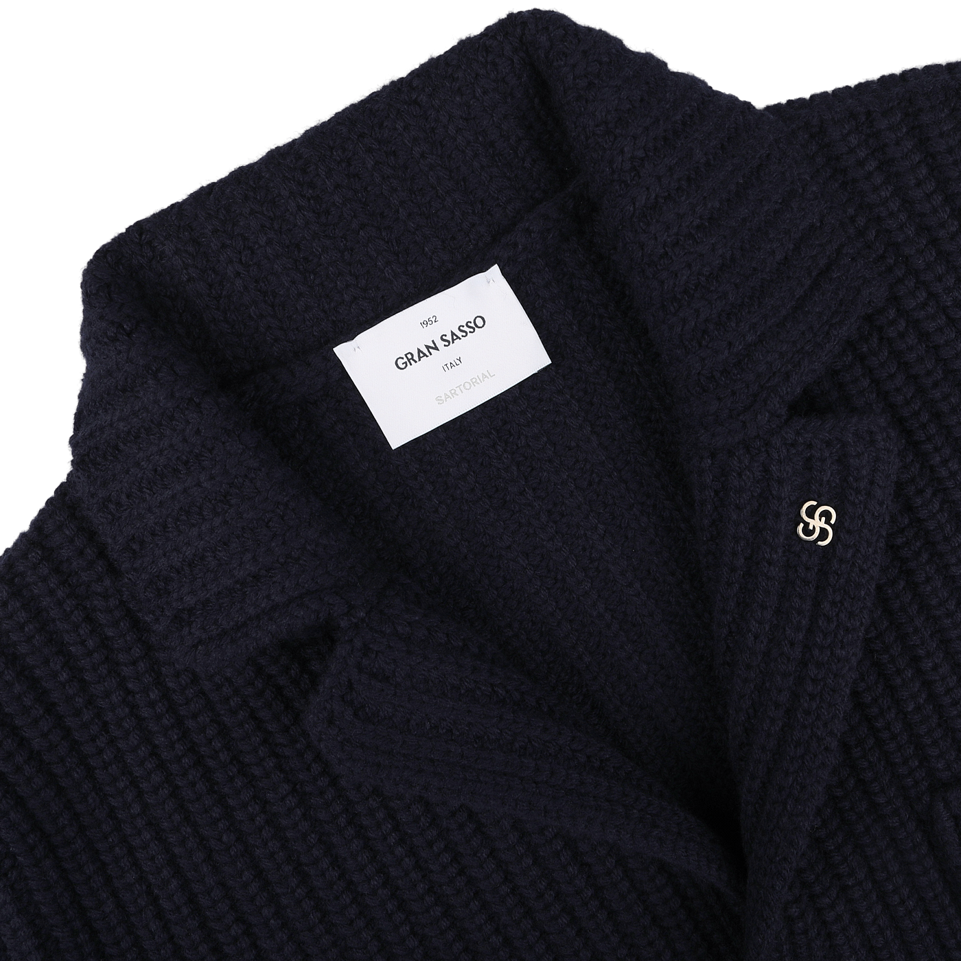 Close-up of a navy blue chunky knitted wool cardigan by Gran Sasso, featuring a metallic pin on the lapel and a white label inside bearing the brand name.