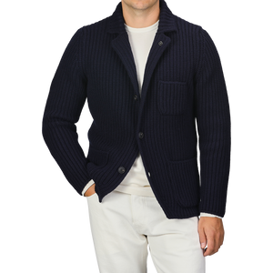 A person wearing a Gran Sasso Navy Blue Chunky Knitted Wool Cardigan over a white shirt and white pants. Their left hand is in their pocket.