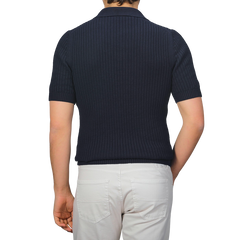 Individual in a navy blue organic cotton polo shirt by Gran Sasso and white pants, seen from behind against a gray background.