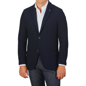 A man wearing a Navy Blue Virgin Wool Sartorial Jacket by Gran Sasso over a white collared shirt and blue jeans. His hands are at his sides against a plain gray background.