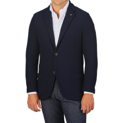 A man wearing a Navy Blue Virgin Wool Sartorial Jacket by Gran Sasso over a white collared shirt and blue jeans. His hands are at his sides against a plain gray background.