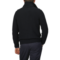 A person wearing a navy blue, textured wool cashmere cardigan by Gran Sasso and dark pants is photographed from the back against a gray background.