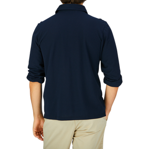 Person wearing a Gran Sasso navy blue slim fit polo shirt, made from cotton jersey and paired with light beige trousers, viewed from the back.