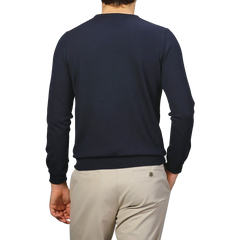 Wearing a Navy Extra Fine Merino Crew Neck by Gran Sasso and beige pants, a person stands against a gray background, adding cozy elegance to their wardrobe.