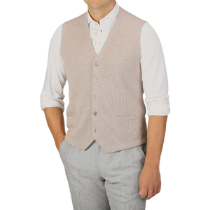 A person wearing a Gran Sasso Oatmeal Beige Knitted Merino Wool Waistcoat over a white long-sleeve shirt with rolled-up sleeves and light gray pants.